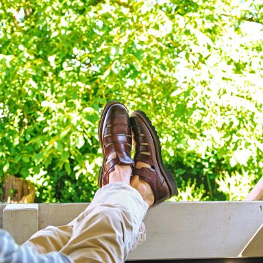 Braune Lederschuhe auf einem Balkongeländer, umgeben von grünem Blätterwerk.