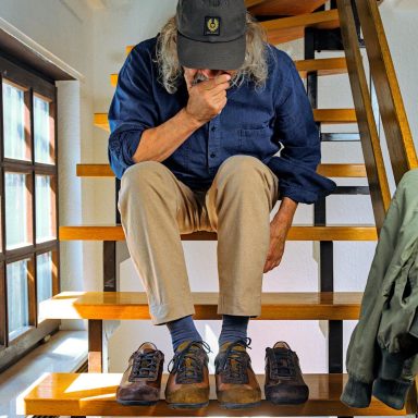 Ein Mann sitzt auf einer Treppe und betrachtet zwei Paare von Schuhen.