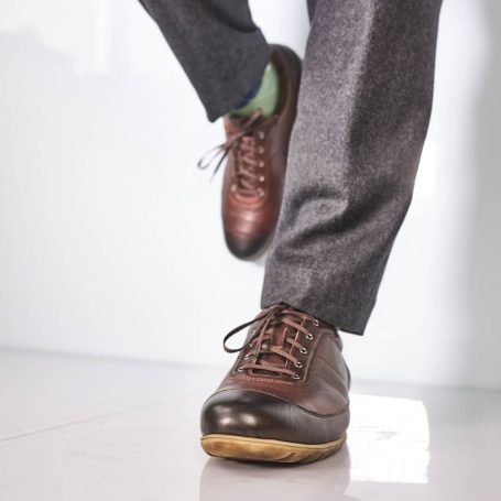 Braune Lederhalbschuhe mit grauen Hosen und grünen Socken.
