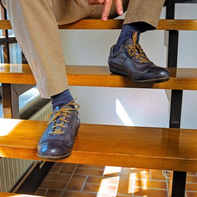 Schwarze Schuhe mit blauen Socken auf Holzstufen. Person macht Peace-Zeichen.
