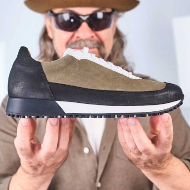 Person hält einen sportschuh mit einer Mischung aus grünem und schwarzem Obermaterial.