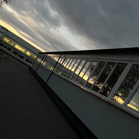 Ein Gebäude mit großen Fenstern, umgeben von grauem Himmel und schwachem Licht.